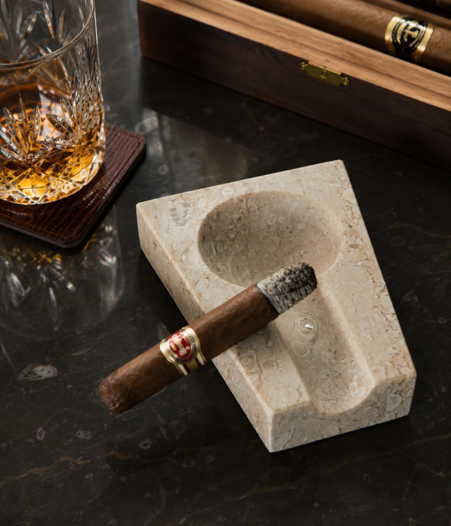 Luxury marble cigar ashtray crafted from Ujungpandang marble with integrated cigar rest displayed beside a whiskey glass and cigar box.